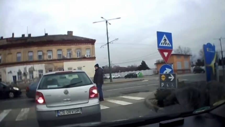 Captură de pe o cameră de bord care surprinde momentul în care un pieton evită la limită un autoturism pe trecere.