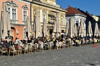 Oameni relaxându-se la mesele unei terase dintr-o piață istorică din Timișoara într-o zi însorită de primăvară