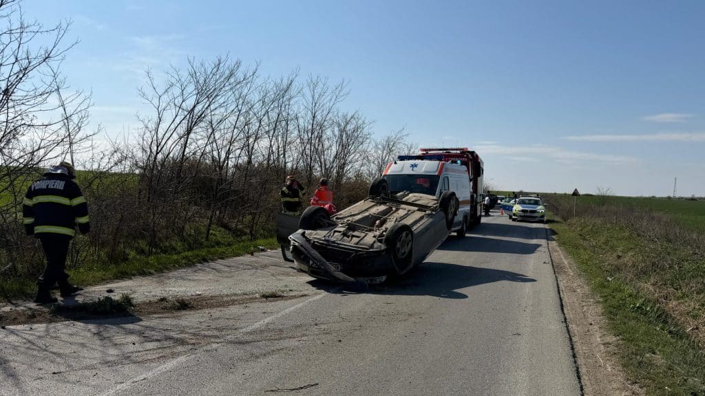 Autoturism cu avarii majore răsturnat pe plafon în afara părții carosabile pe marginea unui drum național.