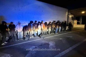 Polițiști de frontieră verificând compartimentul de marfă al unui TIR, unde au fost descoperite persoane ascunse printre baloturi de materiale textile.