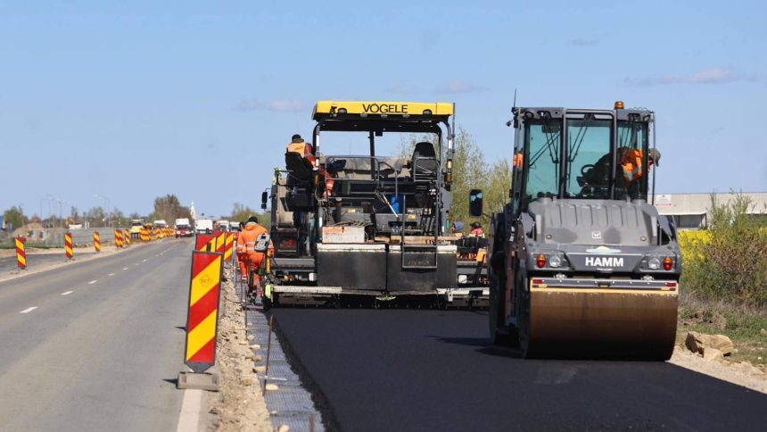 Finisor de asfalt și cilindru compactor lucrând pe sectorul lărgit la patru benzi al drumului județean care leagă Timișoara de Sânandrei.