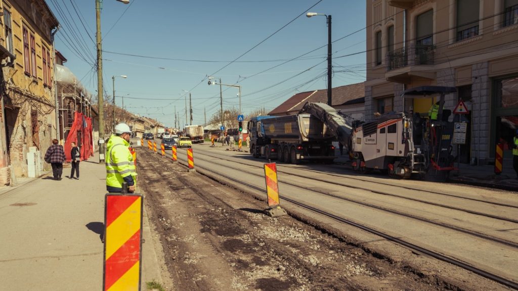 Muncitori sortând și curățând manual blocurile de piatră cubică scoase din pavajul Pieței Traian pentru a fi refolosite.