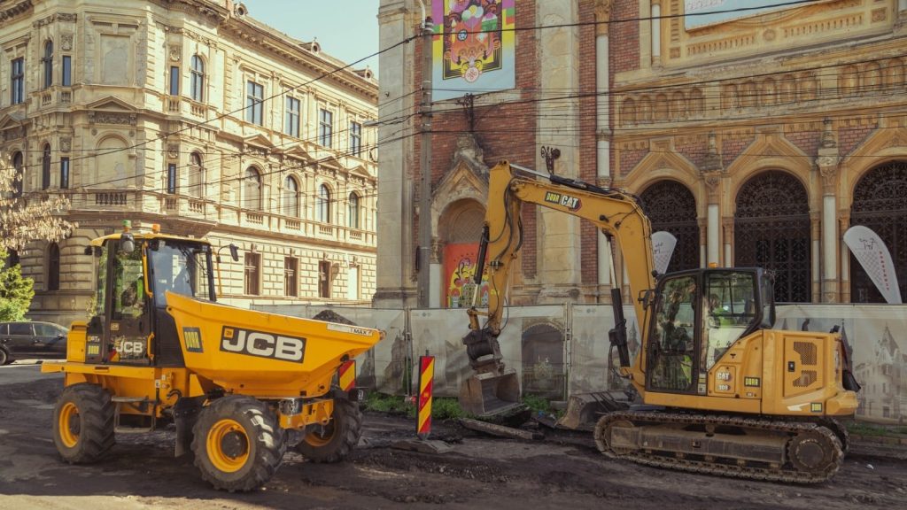 Muncitori sortând și curățând manual blocurile de piatră cubică scoase din pavajul Pieței Traian pentru a fi refolosite.