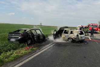 Echipaje de pompieri stingând o mașină cuprinsă de flăcări pe marginea drumului DN 59C, în timp ce elicopterul SMURD aterizează în apropiere.