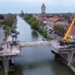 Utilaje masive demontând grinzile de beton ale Podului Muncii de peste canalul Bega din Timișoara.