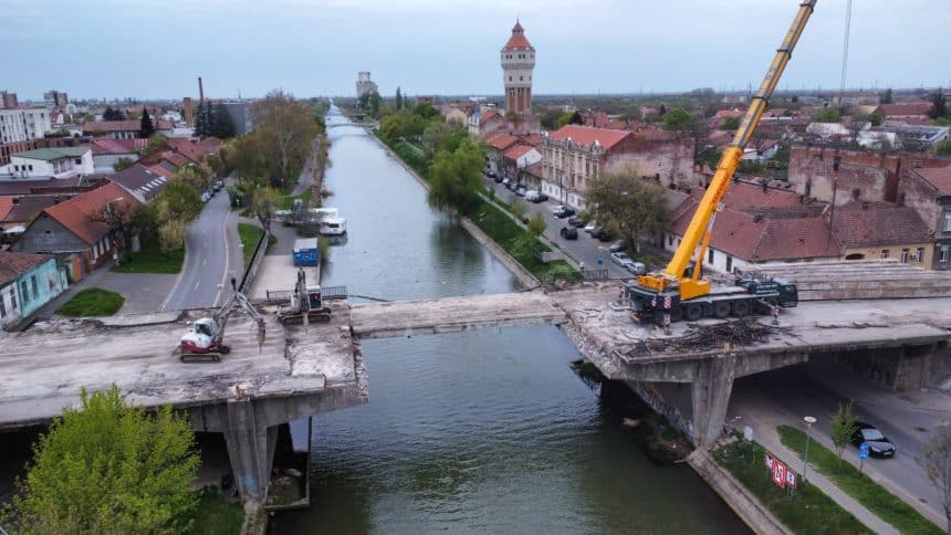 Utilaje masive demontând grinzile de beton ale Podului Muncii de peste canalul Bega din Timișoara.
