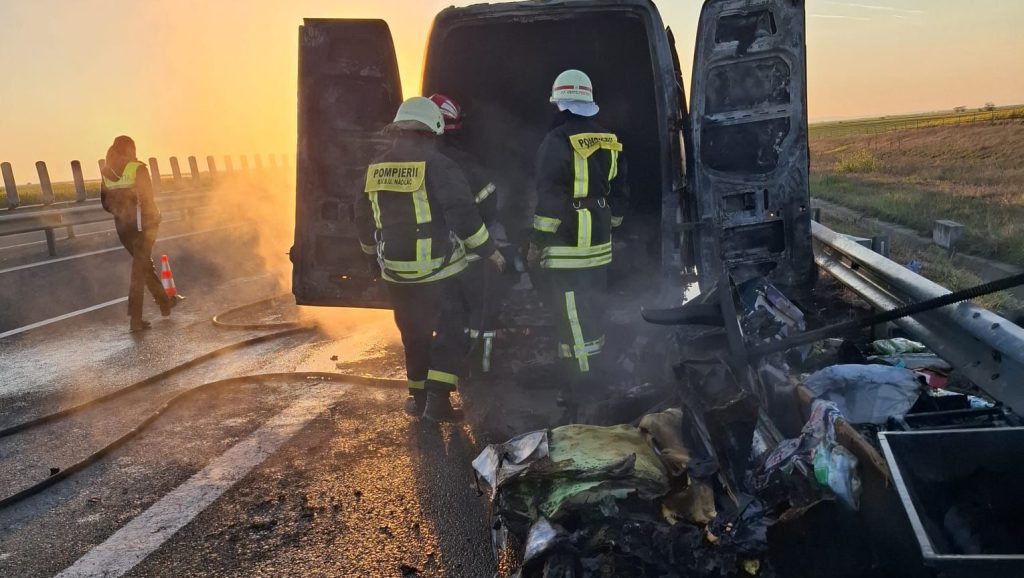 Pompieri stingând flăcările la o autoutilitară de transport mobilier pe banda de urgență a autostrăzii A1.