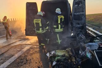 Pompieri stingând flăcările la o autoutilitară de transport mobilier pe banda de urgență a autostrăzii A1.