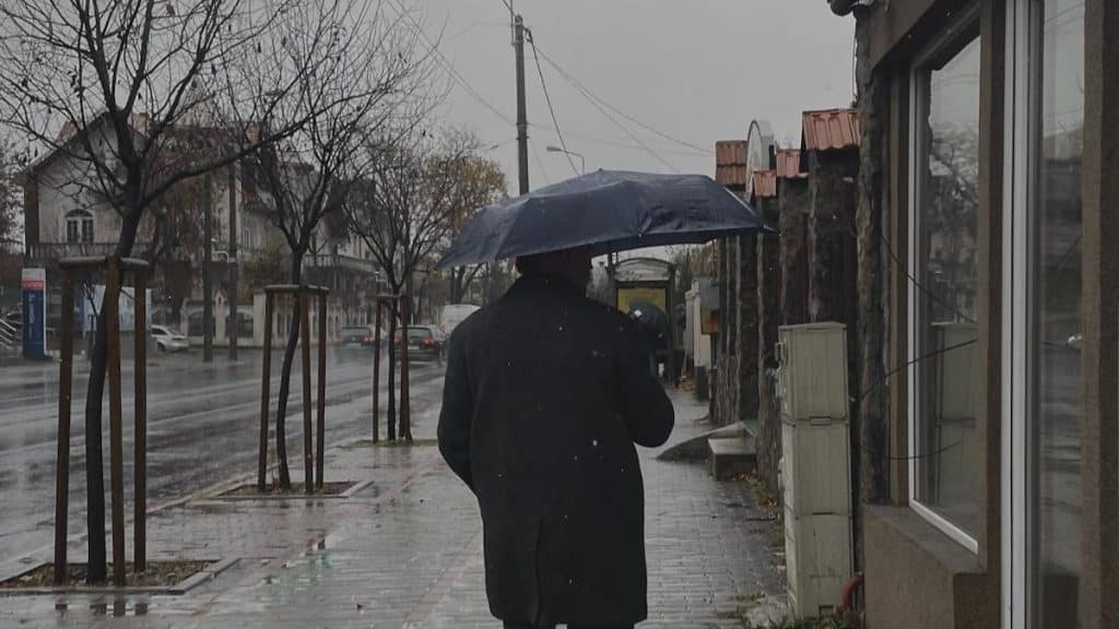 Locuitori din Timișoara mergând prin ploaie cu umbrele și cizme de cauciuc după o răcire bruscă a vremii.