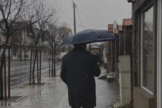 Locuitori din Timișoara mergând prin ploaie cu umbrele și cizme de cauciuc după o răcire bruscă a vremii.