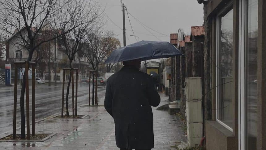 Locuitori din Timișoara mergând prin ploaie cu umbrele și cizme de cauciuc după o răcire bruscă a vremii.