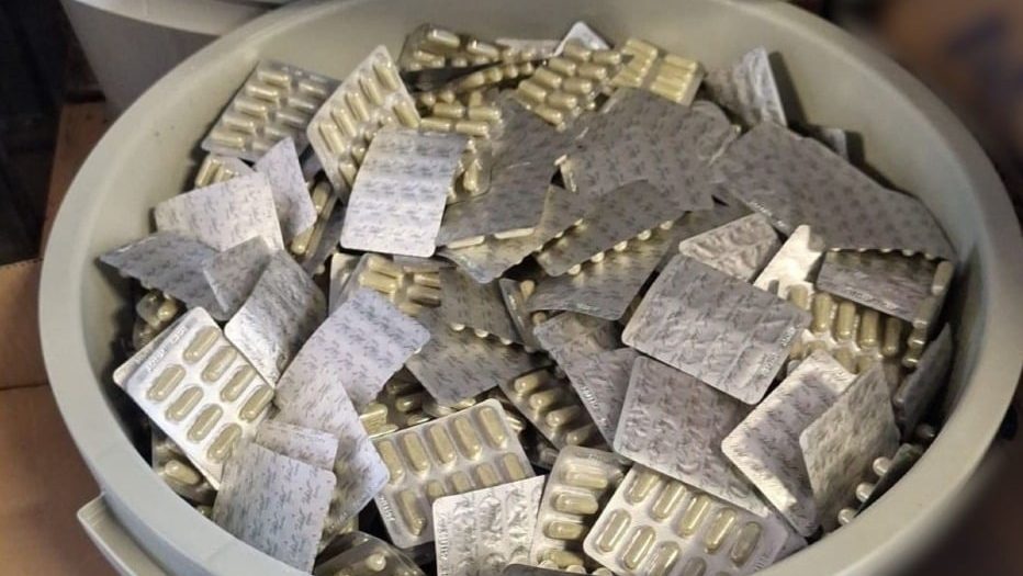 Polițiști și procurori DIICOT examinând sute de cutii cu suplimente alimentare false confiscate în urma perchezițiilor din mai 2026.
