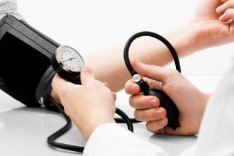 Un cadru medical măsurând tensiunea arterială a unui pacient cu ajutorul unui tensiometru într-un cabinet de cardiologie.