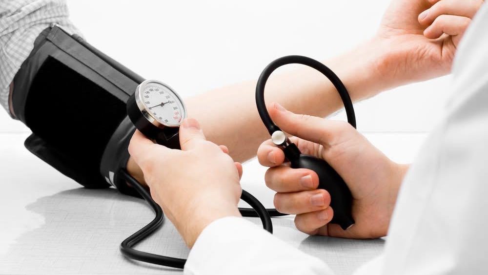 Un cadru medical măsurând tensiunea arterială a unui pacient cu ajutorul unui tensiometru într-un cabinet de cardiologie.