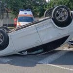 Un autoturism răsturnat pe plafon în mijlocul unei intersecții din Timișoara, înconjurat de echipaje de intervenție și bucăți de caroserie.