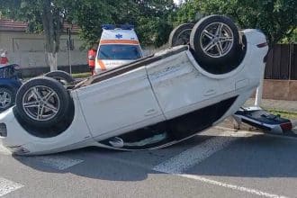 Un autoturism răsturnat pe plafon în mijlocul unei intersecții din Timișoara, înconjurat de echipaje de intervenție și bucăți de caroserie.