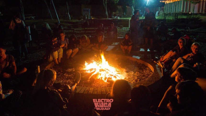 Participanți la festivalul Electroruga din satul Buzad relaxându-se pe iarbă în fața scenei principale de la The Village.