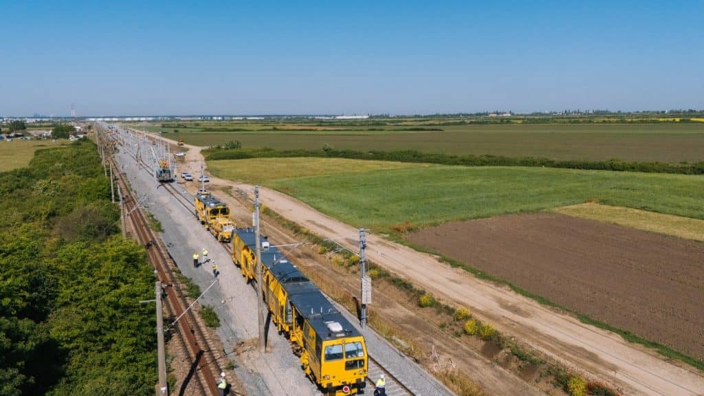 Autocar de transfer pentru călători parcat în fața unei gări CFR din județul Timiș în timpul lucrărilor de reabilitare.