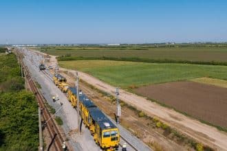 Autocar de transfer pentru călători parcat în fața unei gări CFR din județul Timiș în timpul lucrărilor de reabilitare.
