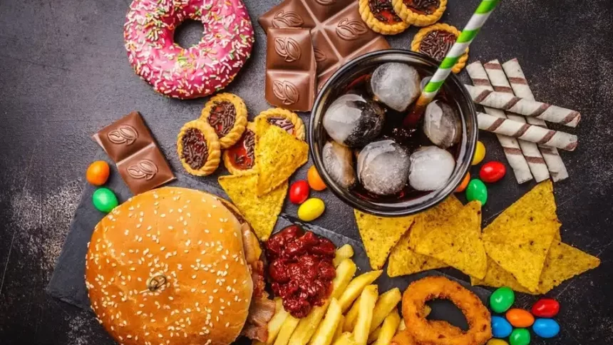 Copil care privește reclame colorate la televizor în timp ce consumă gustări ultraprocesate și băuturi carbogazoase.