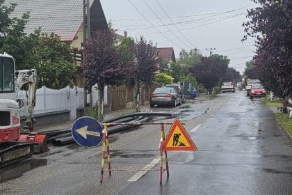 Excavator și utilaje grele efectuând săpături în carosabil pentru montarea unui bazin de canalizare pe o stradă din Dumbrăvița.