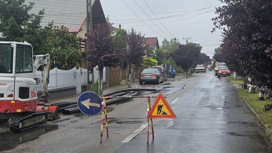 Excavator și utilaje grele efectuând săpături în carosabil pentru montarea unui bazin de canalizare pe o stradă din Dumbrăvița.
