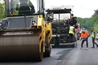 Utilaje grele și finisoare de asfalt turnând un nou strat de rulare pe un sector de drum județean din estul județului Timiș.
