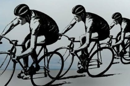 Grup de cicliști în timpul unei curse pe un drum național flancat de echipaje de însoțire ale poliției.