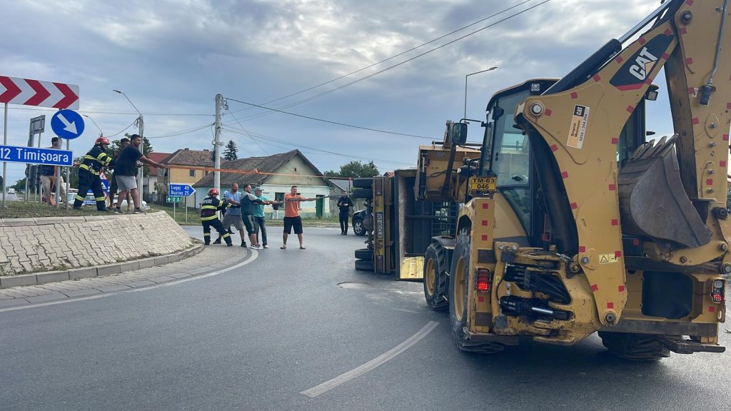 Autoutilitară încărcată cu cherestea răsturnată pe o parte într-un sens giratoriu din Moșnița Nouă, cu materialul lemnos împrăștiat pe șosea.