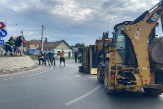 Autoutilitară încărcată cu cherestea răsturnată pe o parte într-un sens giratoriu din Moșnița Nouă, cu materialul lemnos împrăștiat pe șosea.