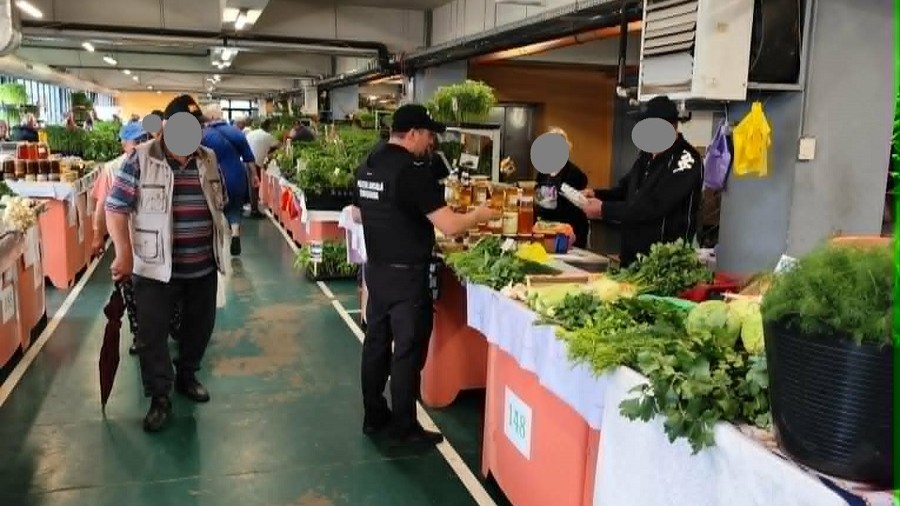 Agenți ai Poliției Locale Timișoara verificând atestatele de producător și cântarele comercianților la o tarabă de legume dintr-o piață agroalimentară.