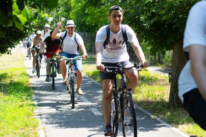 Grup de bicicliști pedalând pe pista de pe malul canalului Bega în cadrul unui eveniment de cicloturism transfrontalier.