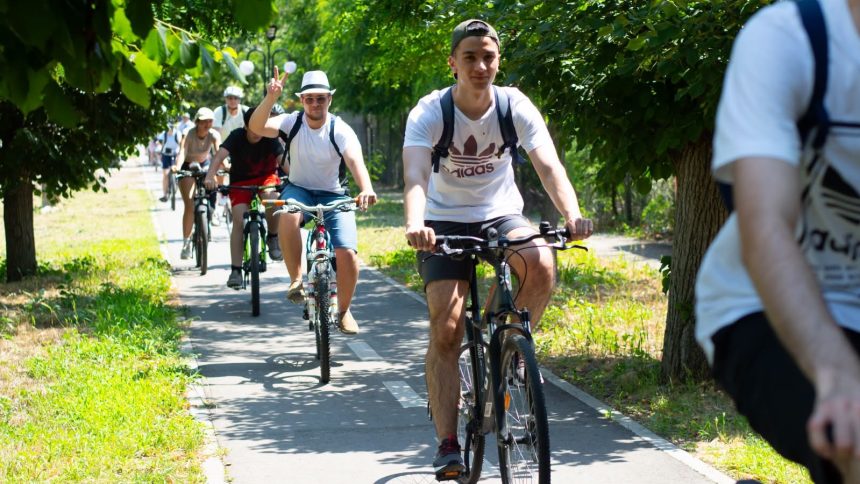 Grup de bicicliști pedalând pe pista de pe malul canalului Bega în cadrul unui eveniment de cicloturism transfrontalier.
