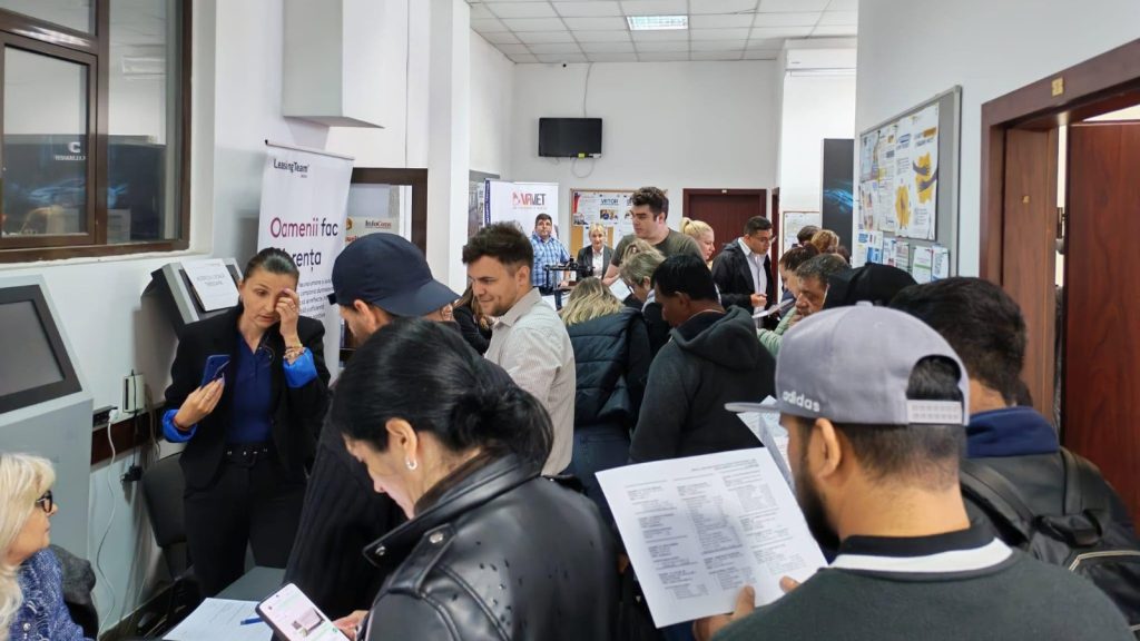 Persoane analizând listele cu locuri de muncă vacante la sediul Agenției pentru Ocuparea Forței de Muncă.