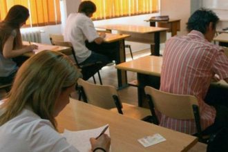 Cadre didactice din județul Timiș susținând proba scrisă a examenului național de titularizare într-o sală de clasă amenajată ca centru de examen.