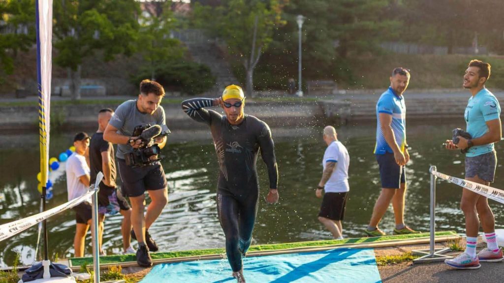 Sportivi concurând la probele de înot pe Bega, ciclism pe bulevarde și alergare în zona centrală, în cadrul evenimentului Timișoara Triathlon.